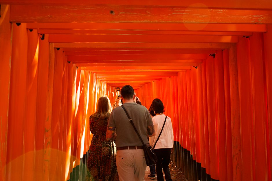 Visitors walking through the vibrant orange torii gates of Fushimi Inari Shrine in Kyoto, Japan.