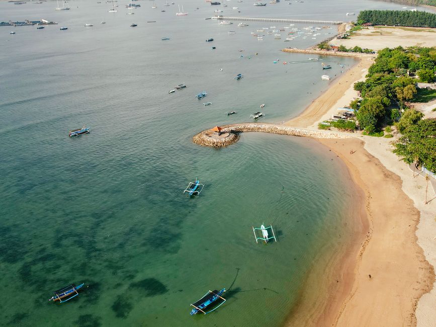 Drone view of a scenic Bali beach with traditional boats and clear waters.