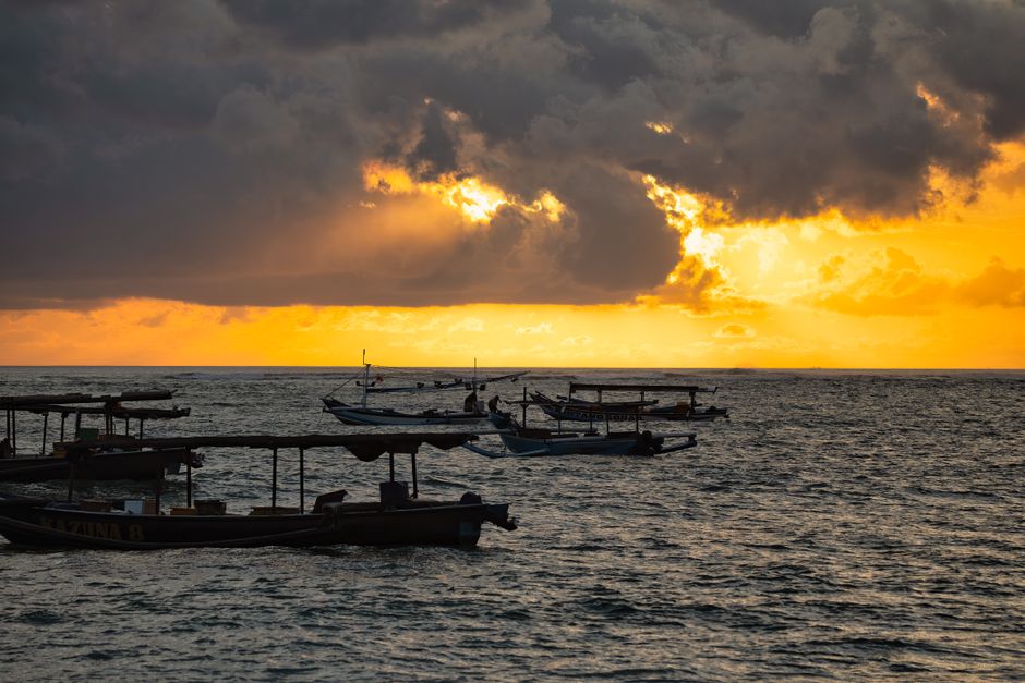 Traditional boats silhouetted at sunset in Bali, Indonesia, capturing a serene seascape.