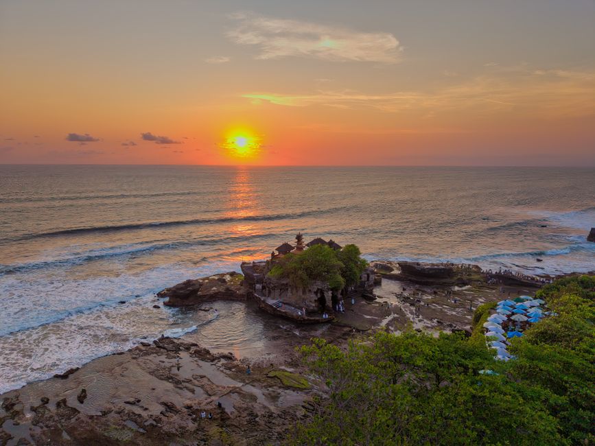 A breathtaking sunset over the iconic Tanah Lot Temple in Bali, Indonesia, casting vibrant reflections on the ocean.