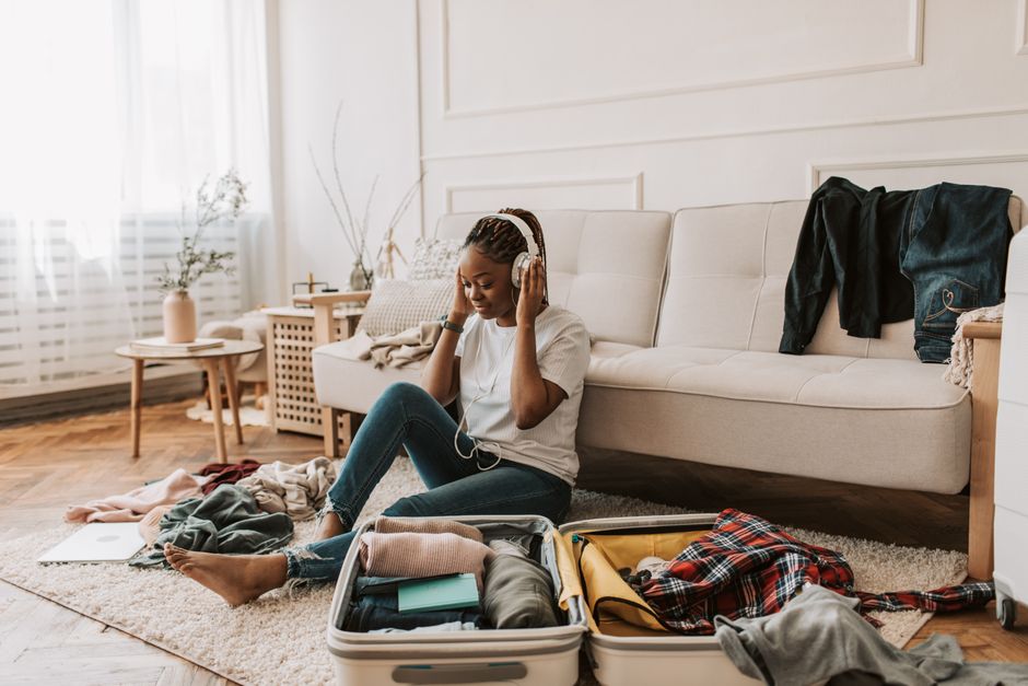 Adult woman packing suitcase while listening to music on headphones at home.
