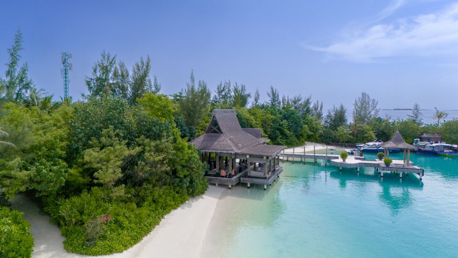 Tranquil beachside resort with a pier in Kaafu Atoll, Maldives, under clear skies.