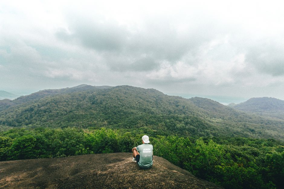 Man observes vast green mountains from a rocky vantage in Ho Chi Minh City, Vietnam.