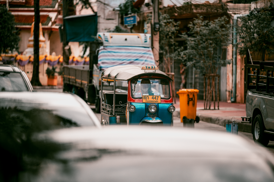 Blue Tuk Tuk navigates busy Bangkok street, vibrant urban scene.