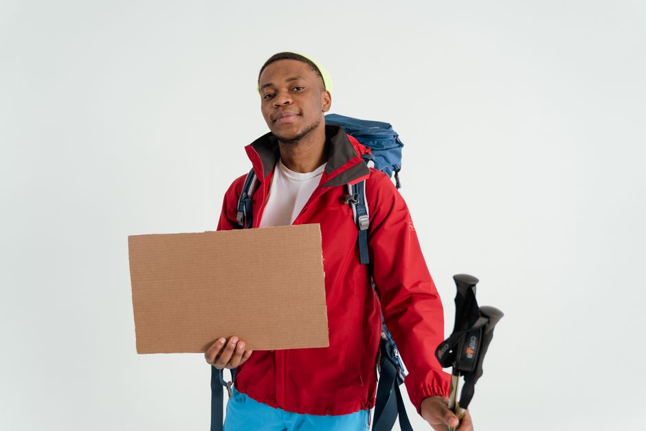 Portrait of a young man hiking with a backpack and cardboard sign, ready for adventure.