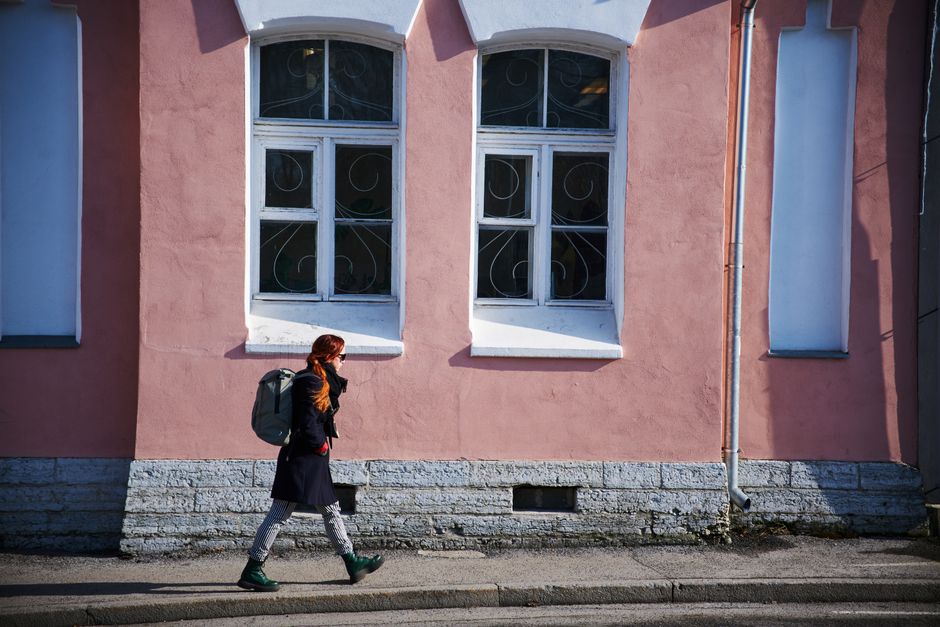 A stylish woman walks by a pastel pink building in Tallinn, Estonia.