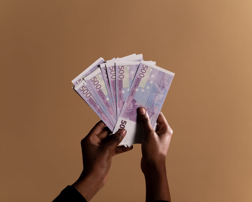 Close-up of hands holding several 500 euro banknotes against a neutral beige background, concept of wealth.
