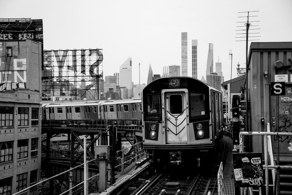 Monochrome image of a subway train with New York City skyline, capturing urban life.