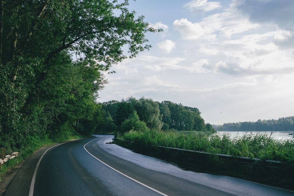 Curved road alongside a river with lush greenery and a serene sky, perfect for travel themes.