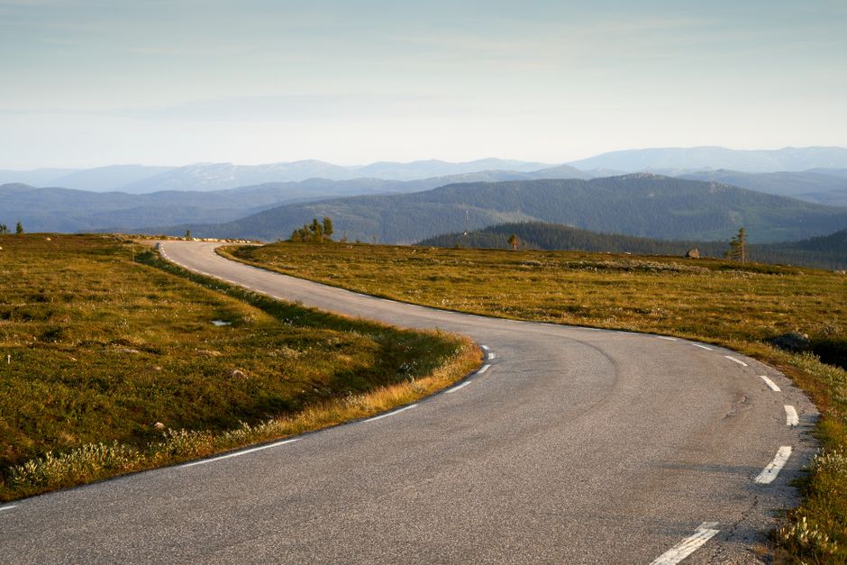 Winding road through peaceful mountain landscape with distant peaks and green terrain.