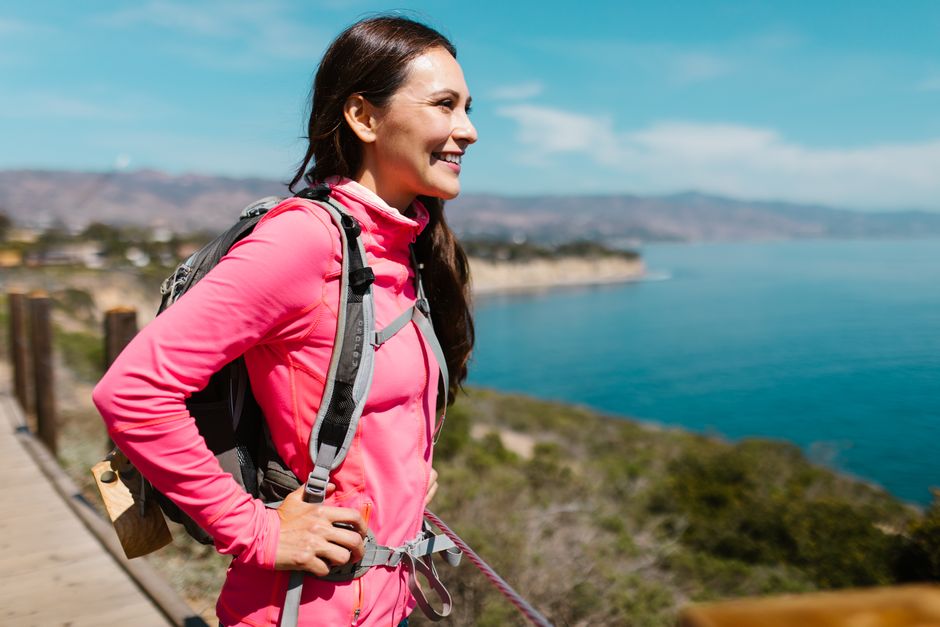 Woman in pink jacket enjoying a coastal hike with ocean view.