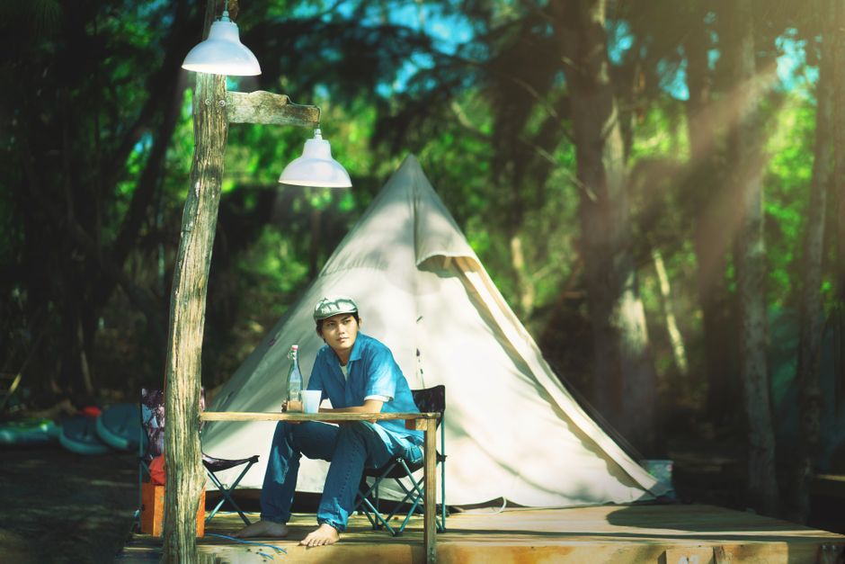 A man sits outside a tent in a forest, enjoying a peaceful camping day.