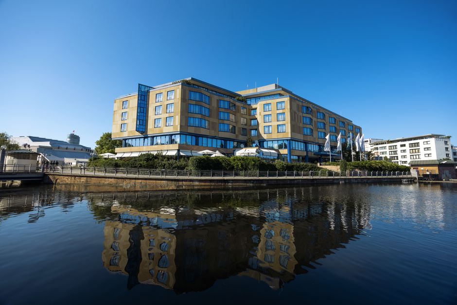 A modern hotel reflecting in a calm water body under a clear blue sky in Pforzheim, Germany.
