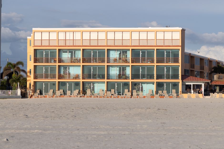 A modern beachfront hotel with balconies, situated on a sandy beach under a clear blue sky.