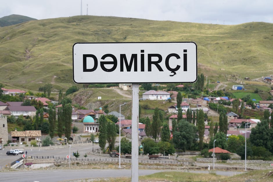Signpost of Demirci village against a hilly landscape, showcasing small houses and lush greenery.