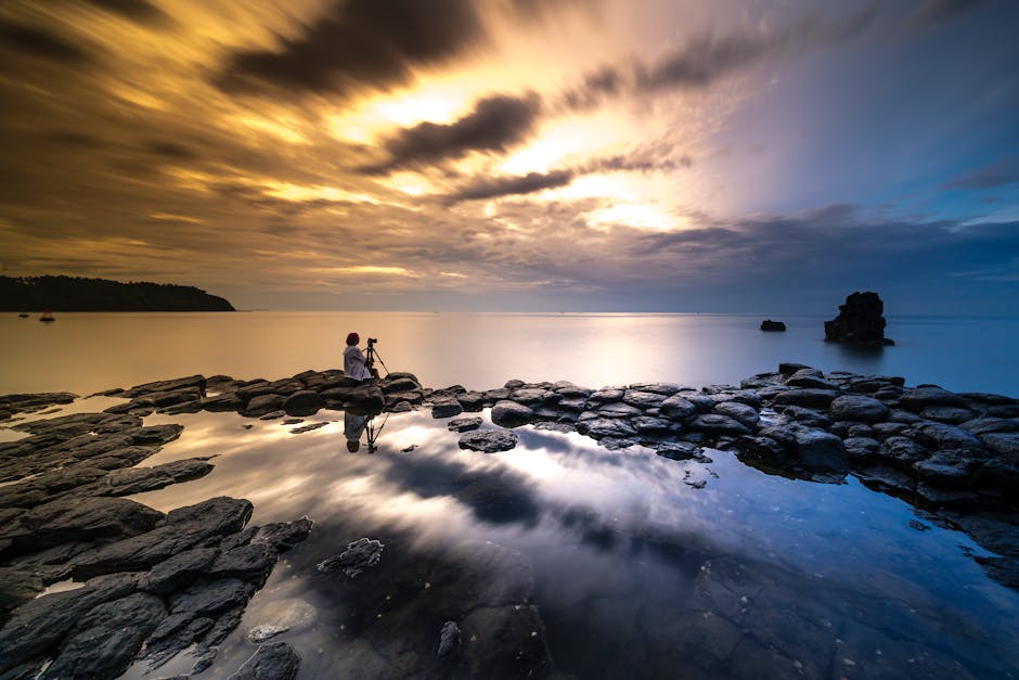 Photographer captures stunning sunset over rocky seashore, reflecting sky in water.