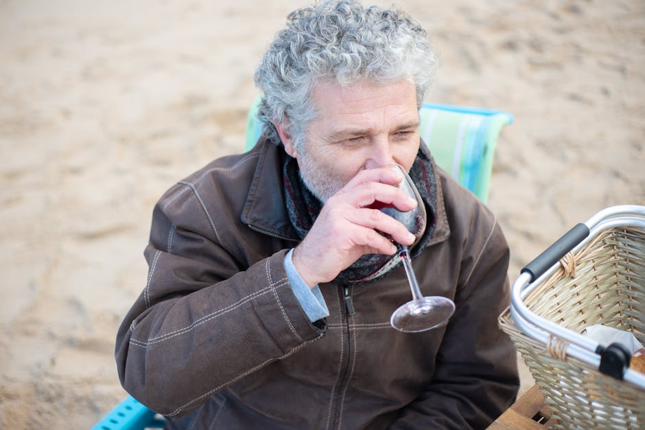 Senior man savoring a glass of red wine on a beach picnic. Relaxed and enjoyable outdoor moment.