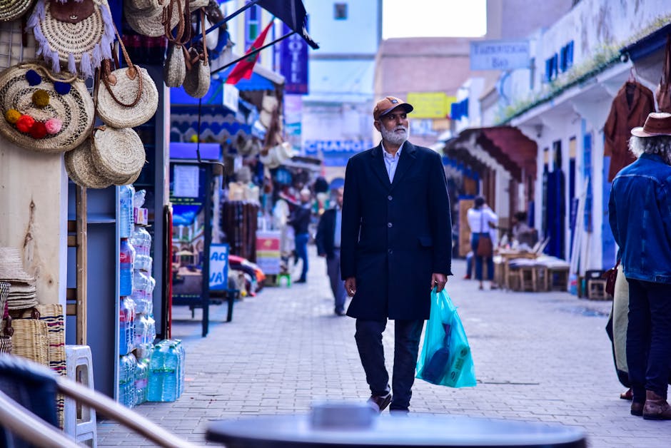 A man walks with a shopping bag in Essaouira market, showing vibrant street life.