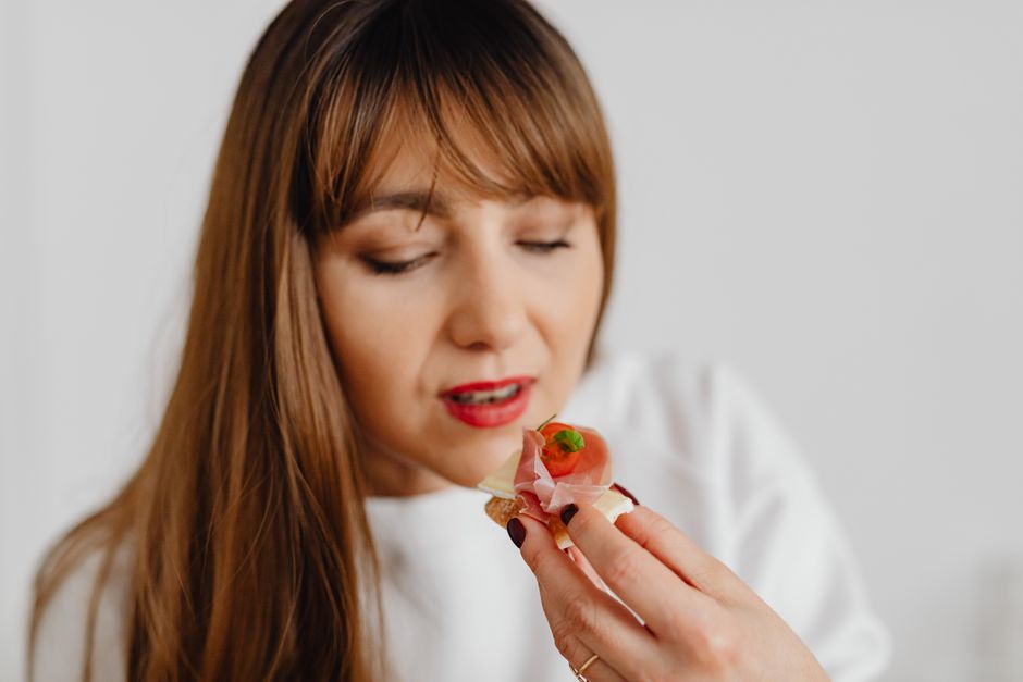 Woman with long hair savoring a gourmet canape indoors.