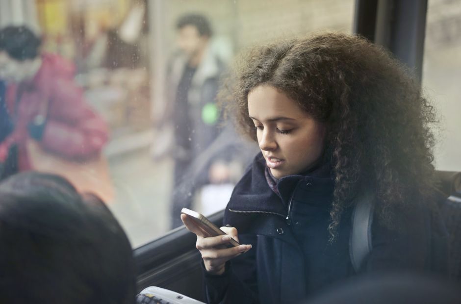 A young woman with curly hair uses her smartphone on a bus.