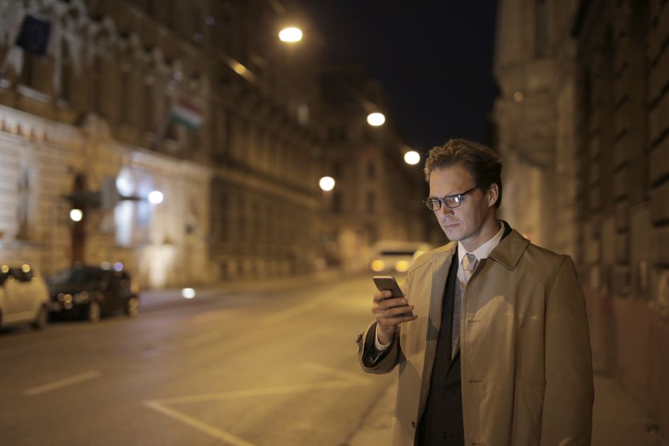 Concentrated adult formally dressed man in glasses surfing internet on cellphone while standing on empty street