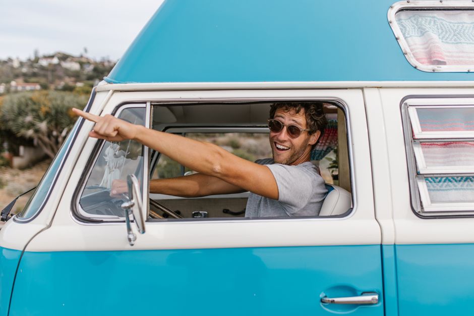 Happy man pointing excitedly from inside a vintage blue van on a sunny day.