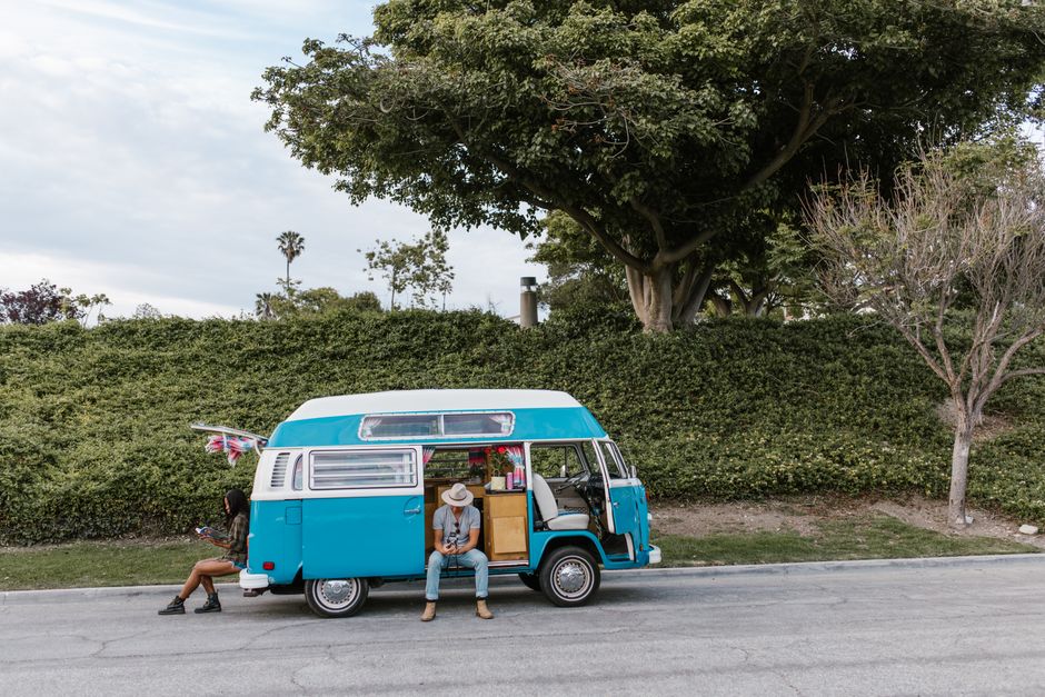 A couple enjoying a sunny day next to a retro blue camper van parked by greenery.