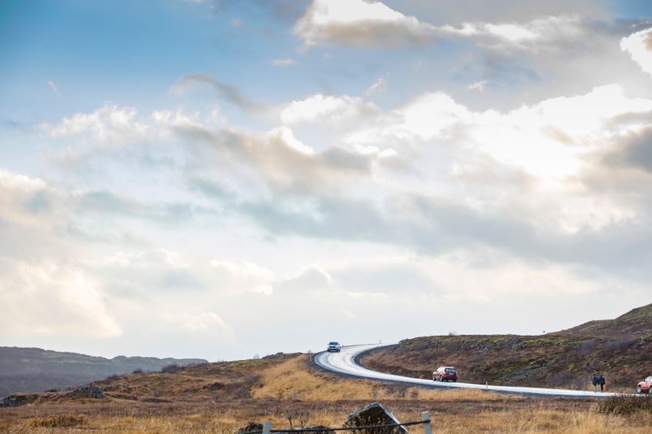 Winding road through countryside with cars, under dramatic cloudy sky. Ideal for travel and exploration themes.