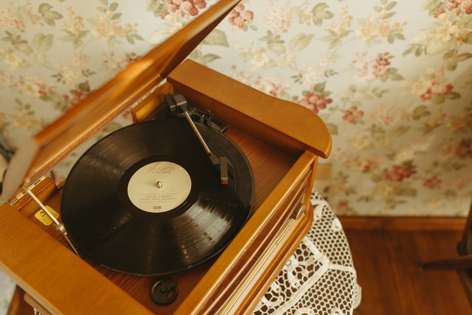 A vintage turntable playing a vinyl record in a cozy, retro interior with floral wallpaper.