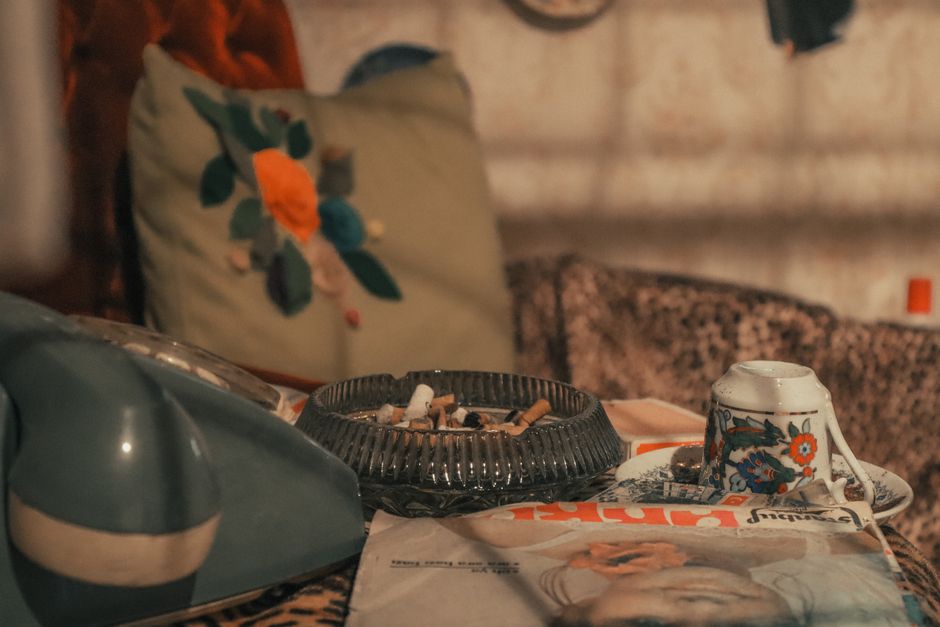 A cozy living room setup with vintage decor featuring a rotary phone, ashtray, and floral cup.