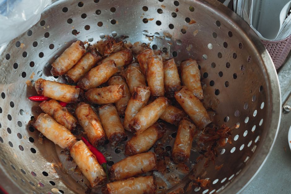 Delicious Vietnamese fried spring rolls with chili peppers in a stainless steel colander.