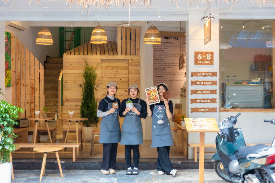 Group of three staff members standing outside a cafe with wooden decor and menu display.